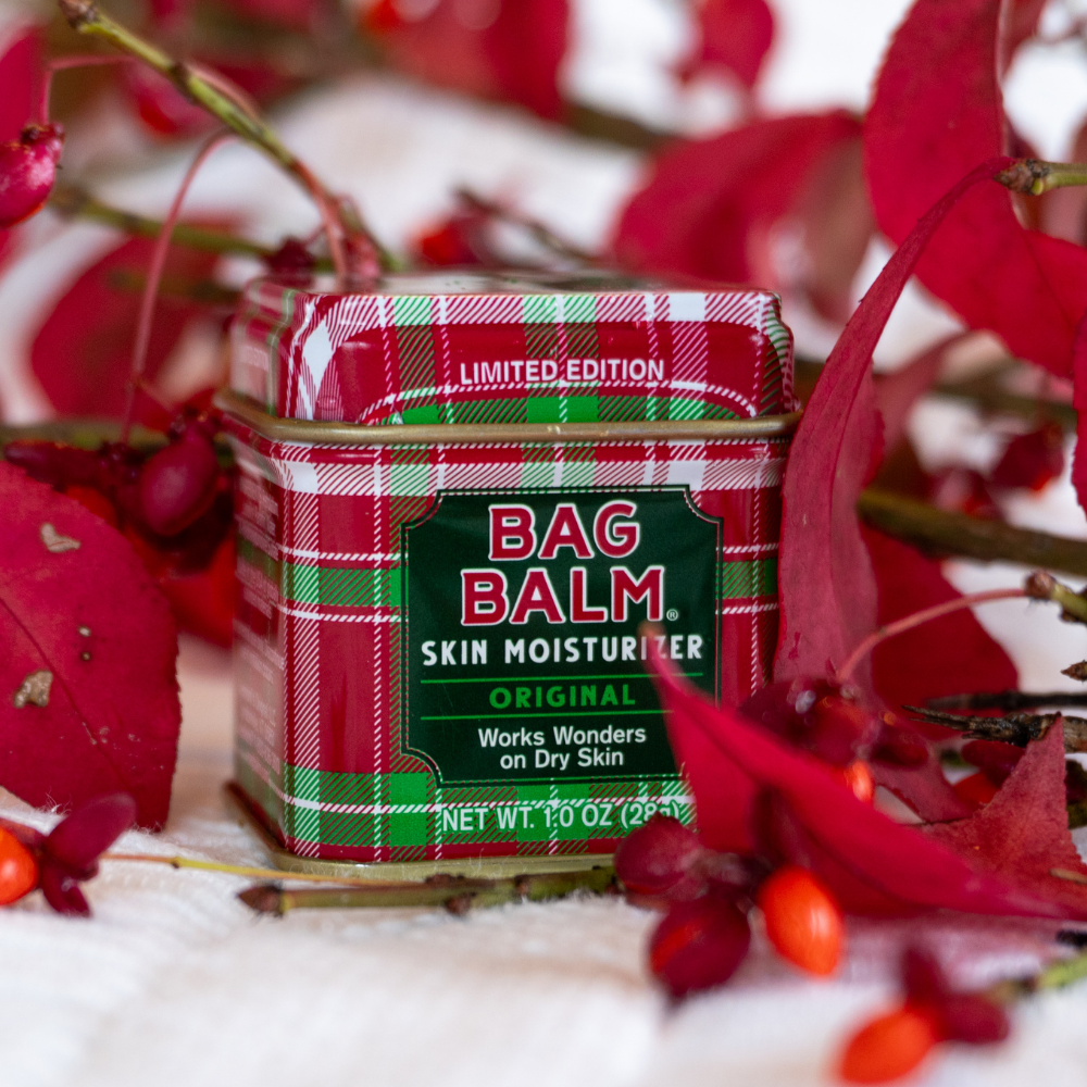 Bag Balm skin moisturizer tin with plaid design surrounded by red leaves and berries