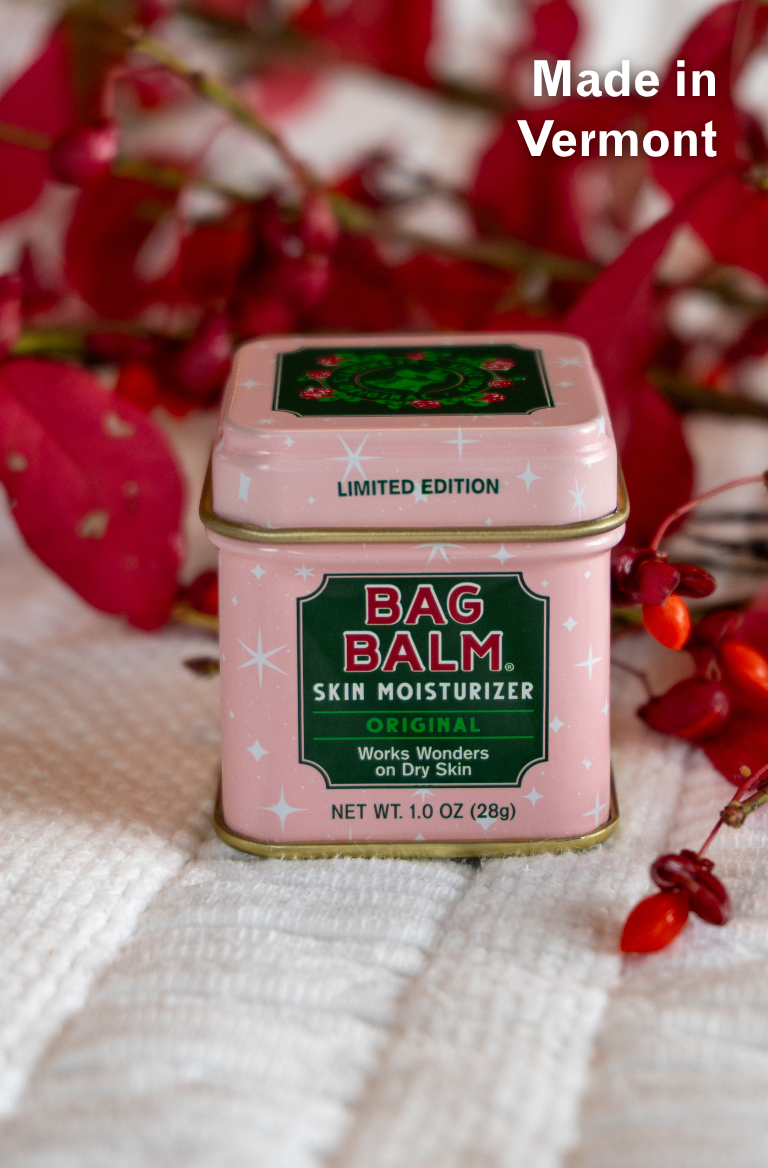 Pink tin of Bag Balm skin moisturizer with red berries in the background
