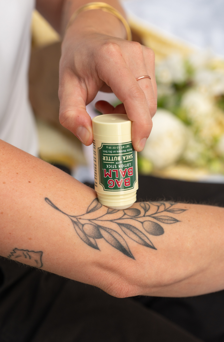 Hand applying Bag Balm Lotion Stick to a tattoo on arm