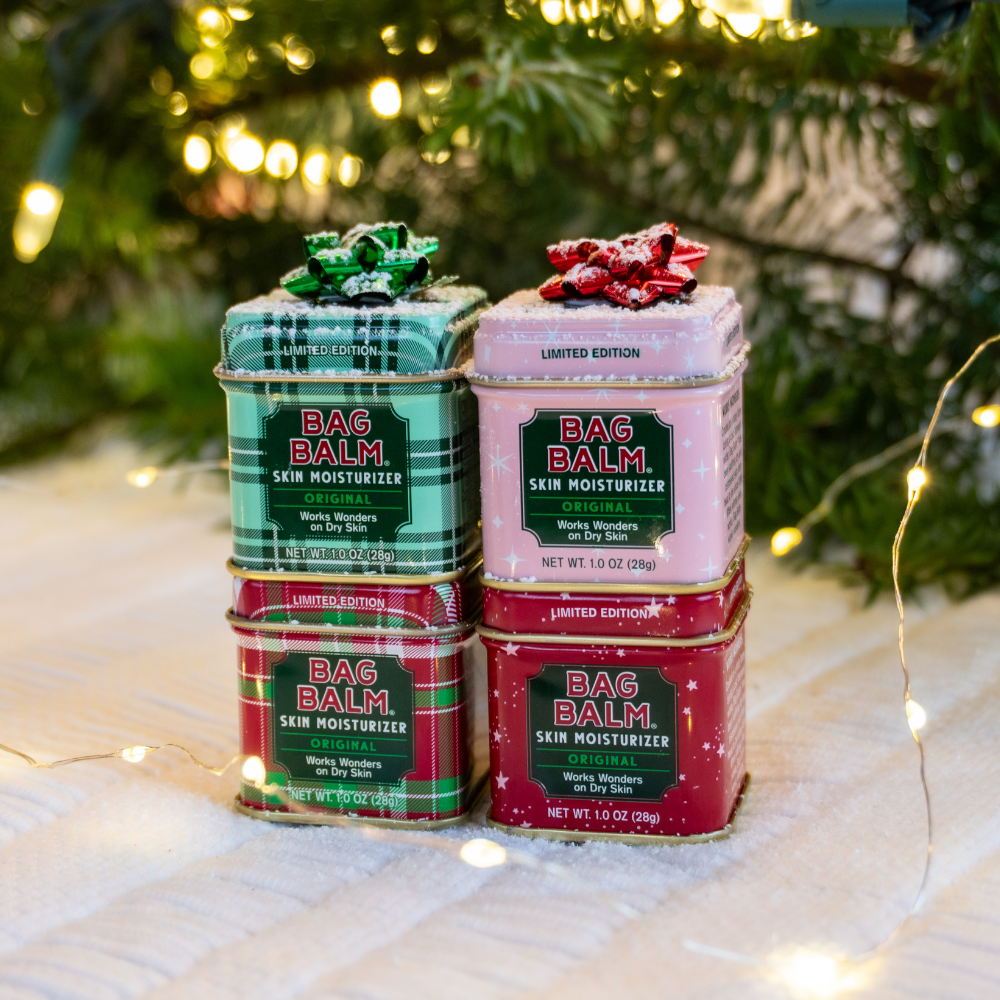 Four tins of Bag Balm skin moisturizer stacked under a Christmas tree with lights.