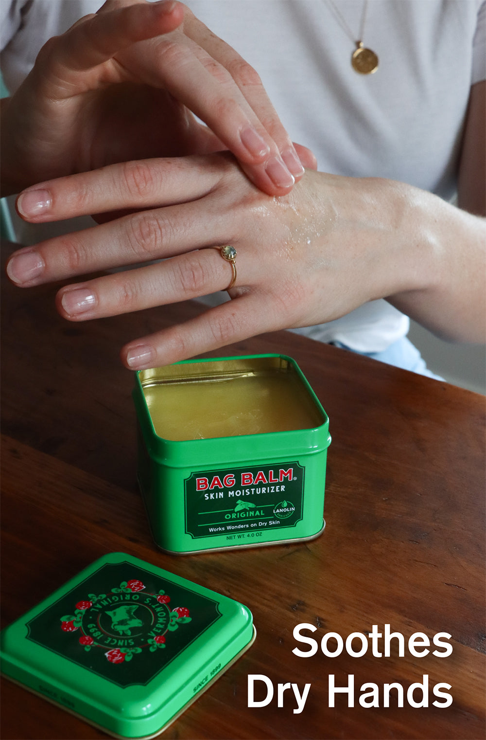 Bag Balm 4oz Tin open with a pair of hands using the ointment