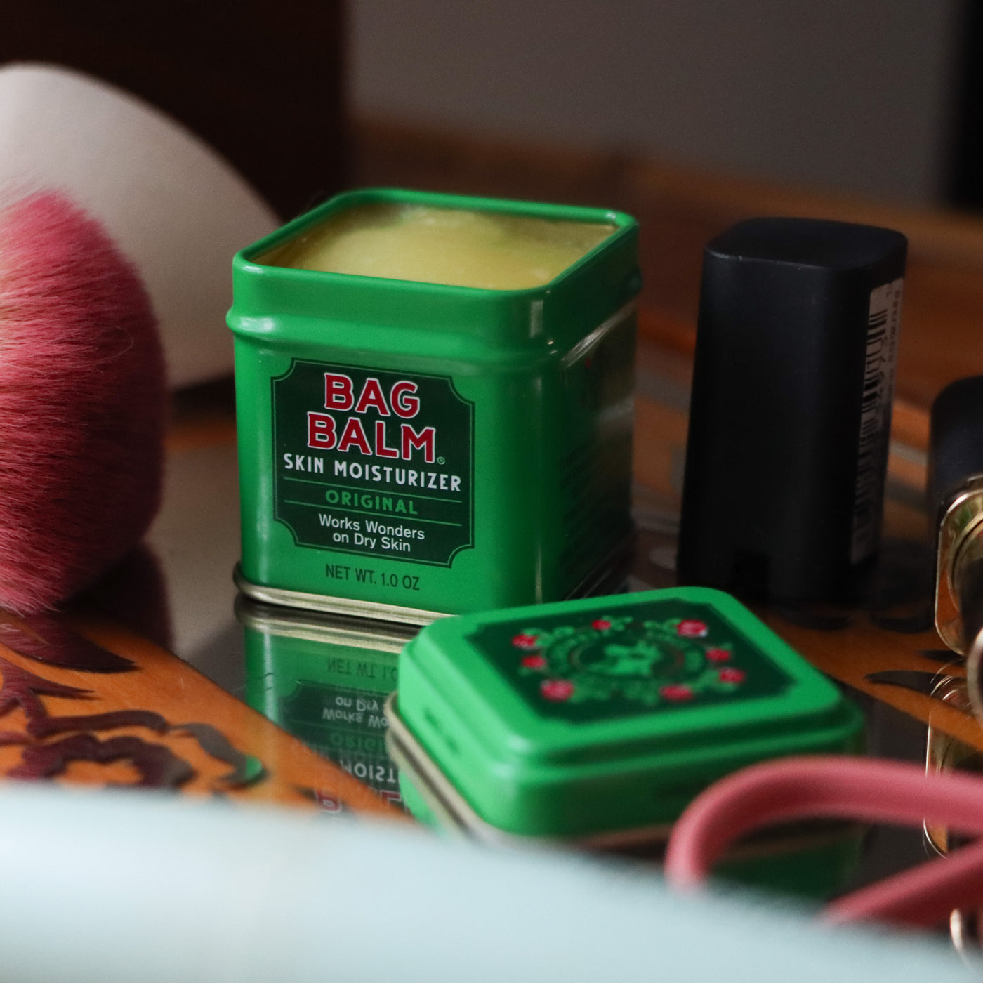 A small, green tin of Bag Balm on a surface