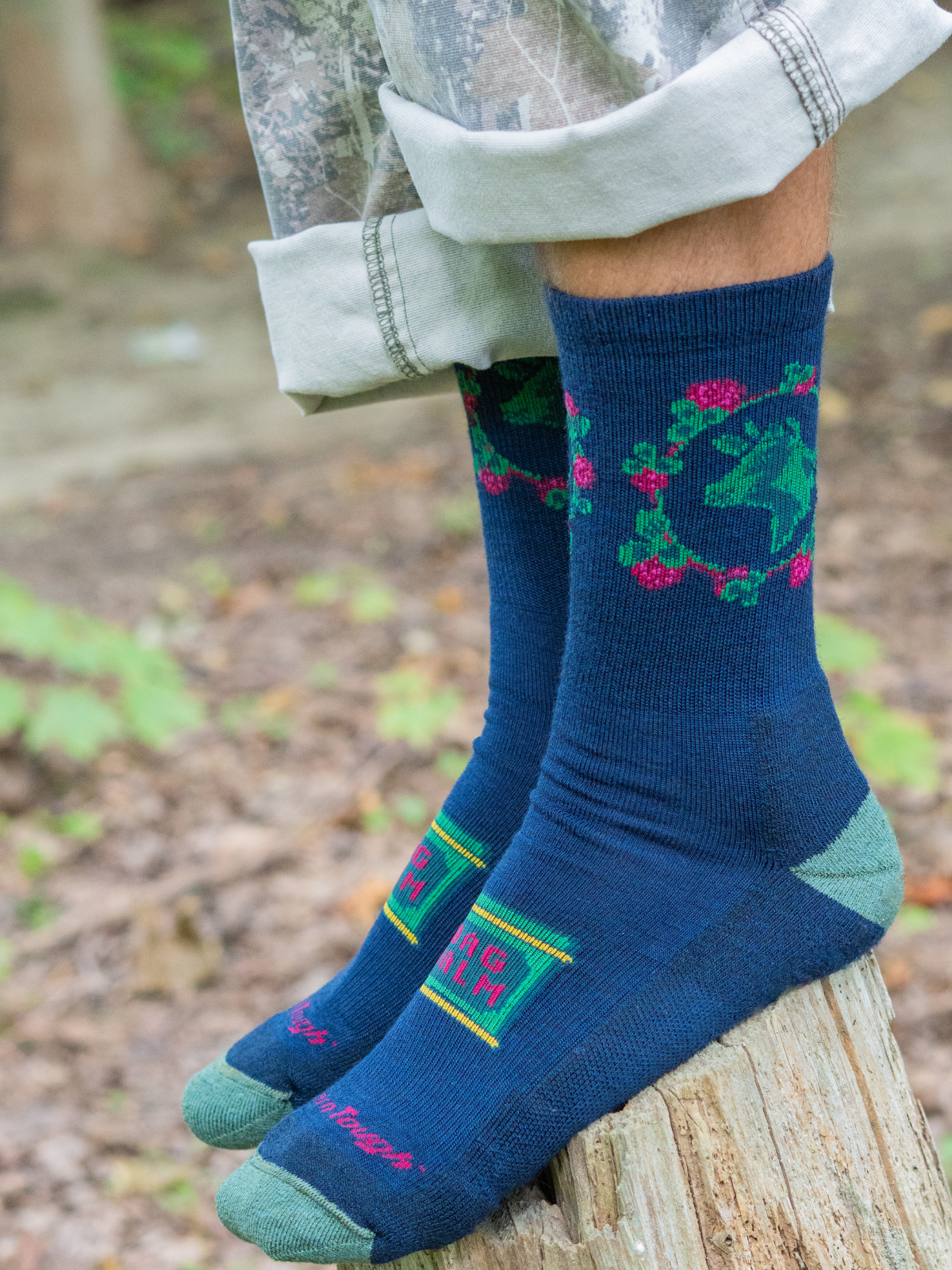 Person wearing Bag Balm socks standing on a wooden log outdoors.