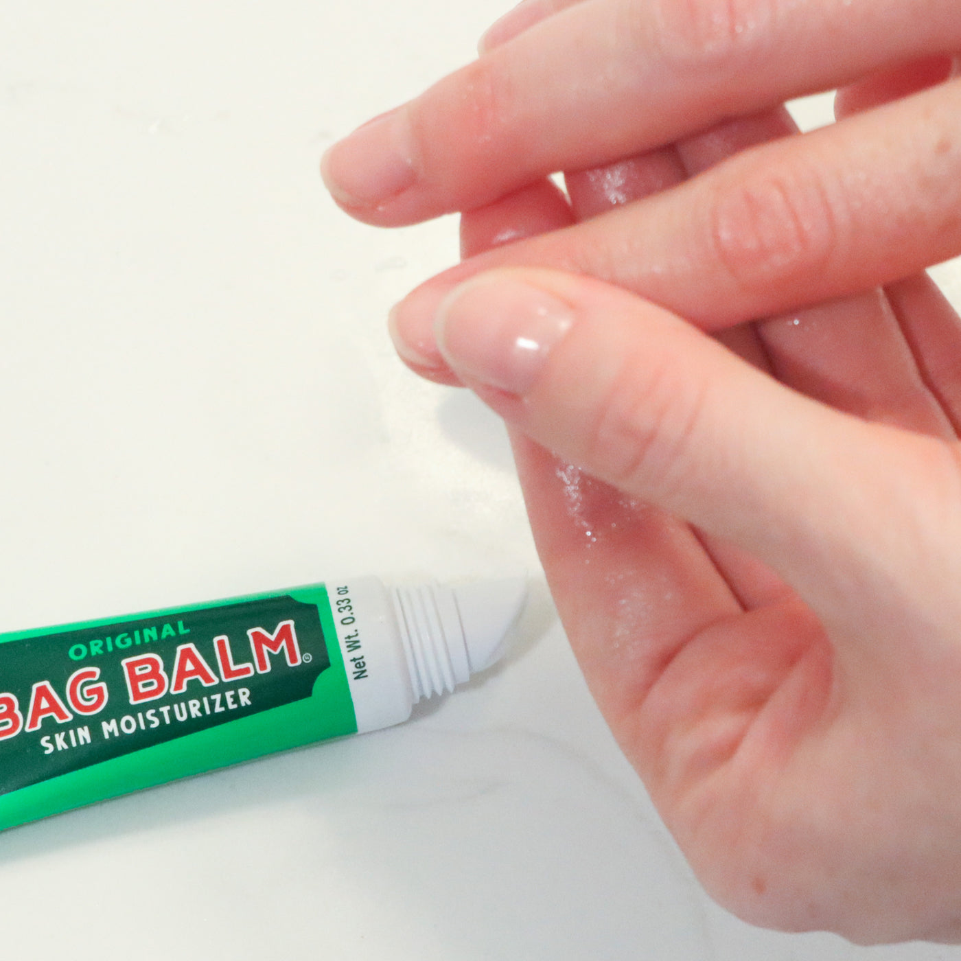 A tube of Bag Balm Skin Moisturizer being applied to a persons cuticles