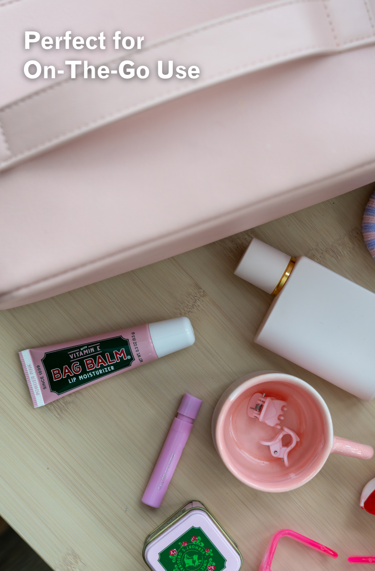 Collection of travel-sized products including a pink bag balm tube, white bottle, and other items on a wooden surface.