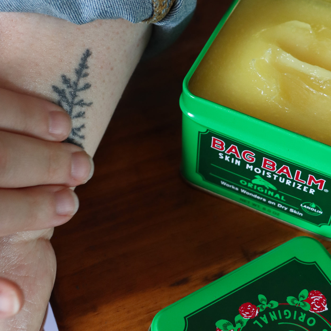 An open tin of Bag Balm being applied to a floral tattoo