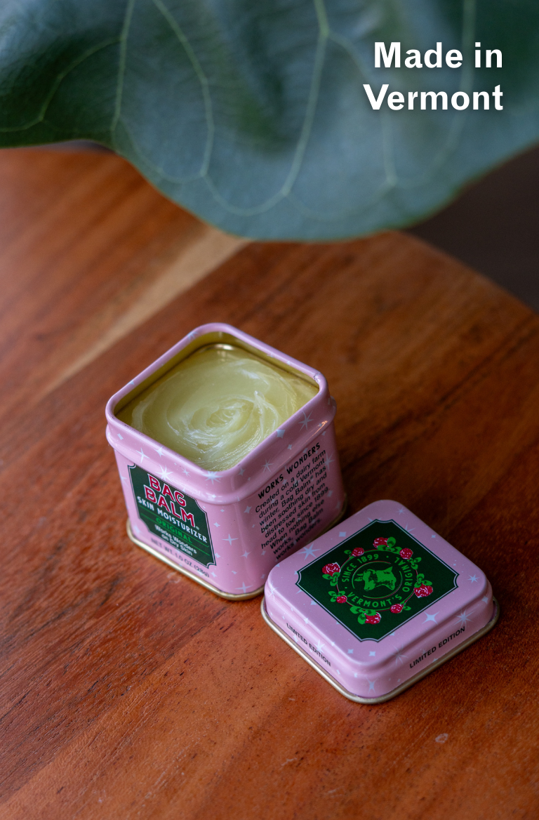 Pink tin of bag balm on a wooden surface, 'Made in Vermont' text above.