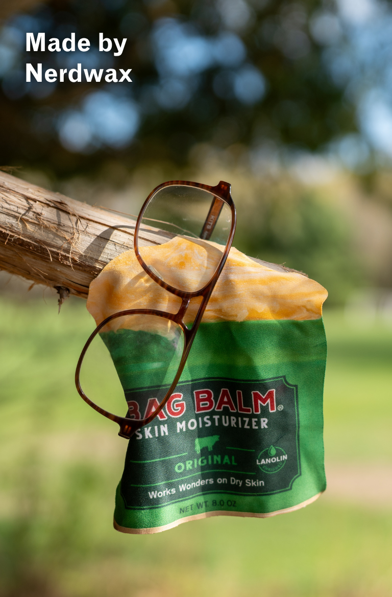 A glasses wipe shaped like a Bag Balm tin and a pair of glasses hanging on a tree branch