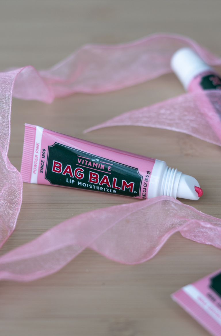 Bag Balm lip balm tube with pink ribbon on a wooden surface