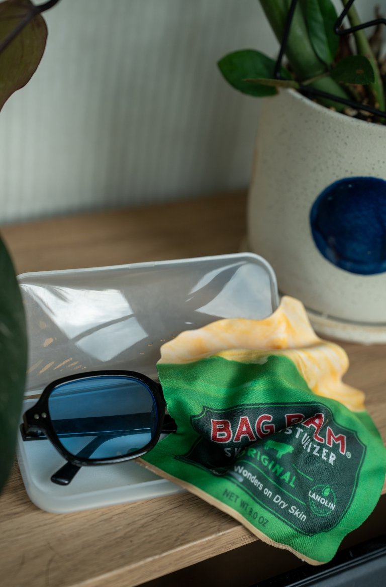 A glasses wipe shaped like a Bag Balm tin laying on top of sunglasses