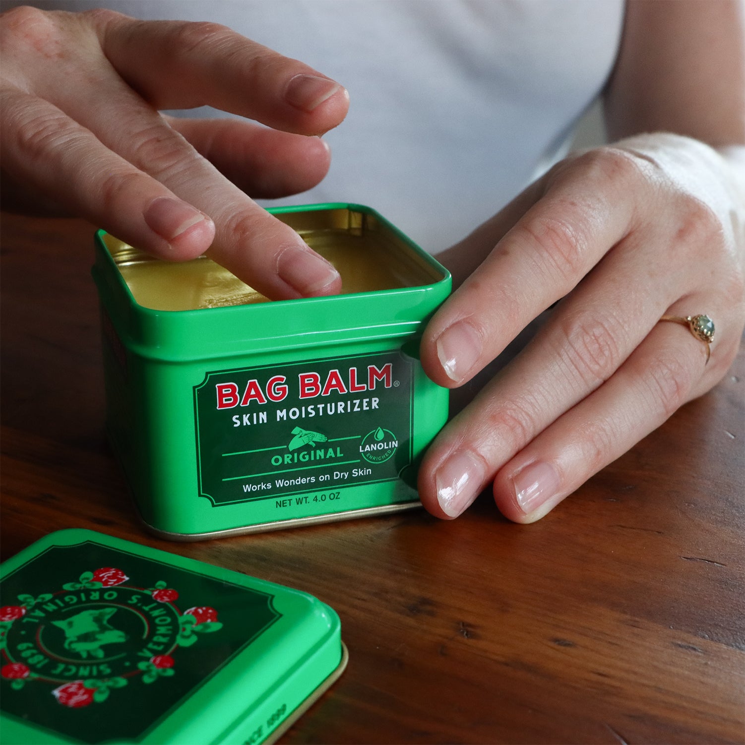 An open tin of Bag Balm with a person's hands reaching in